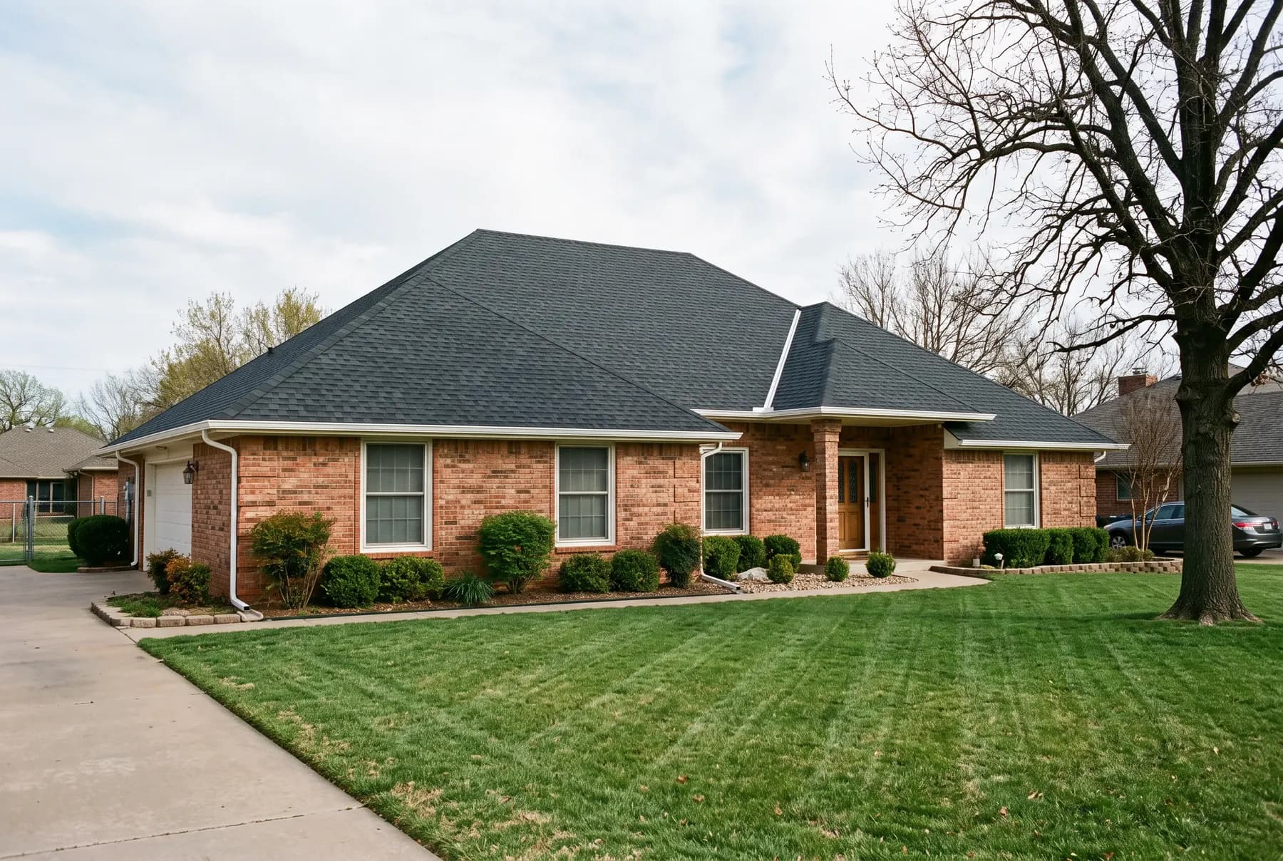 A completed charcoal architectural shingle roof on a suburban Oklahoma brick house.